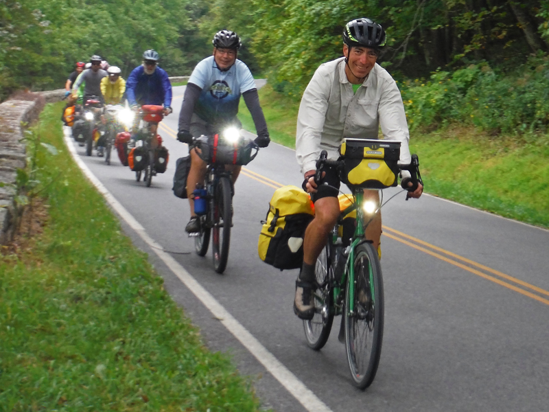 A group of friends riding together on a paved road in single file.